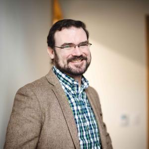 Patrick Cox smiles for a portrait in a hallway.
