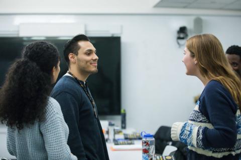 Three graduate students talk in a classroom.